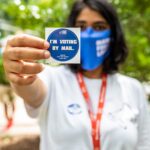 Rhea Wunsch holds up an "I'm voting by mail" sticker