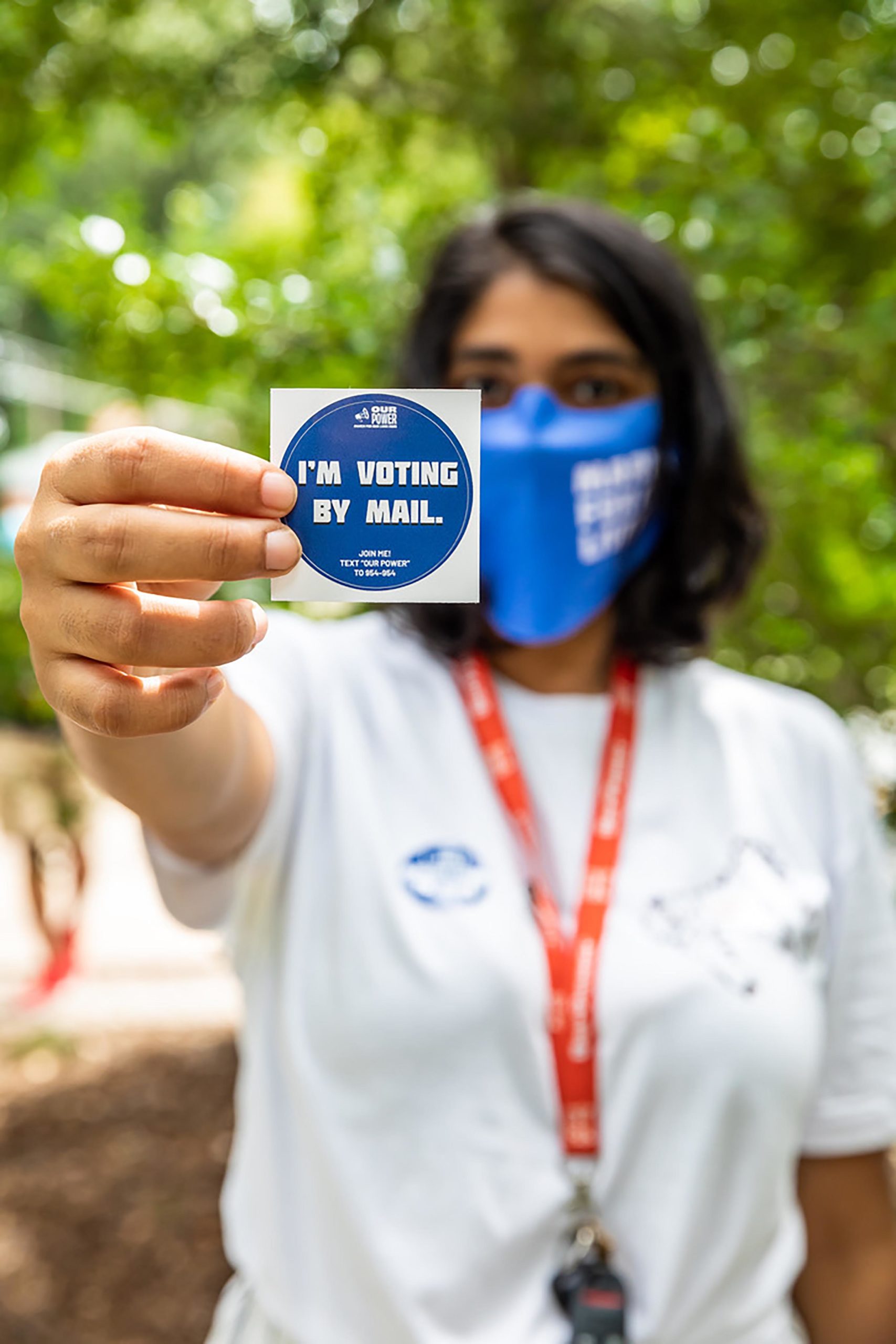 Rhea Wunsch holds up an "I'm voting by mail" sticker