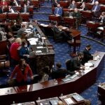 Image of a look inside the impeachment trial. Many people sitting at desks reviewing documents.