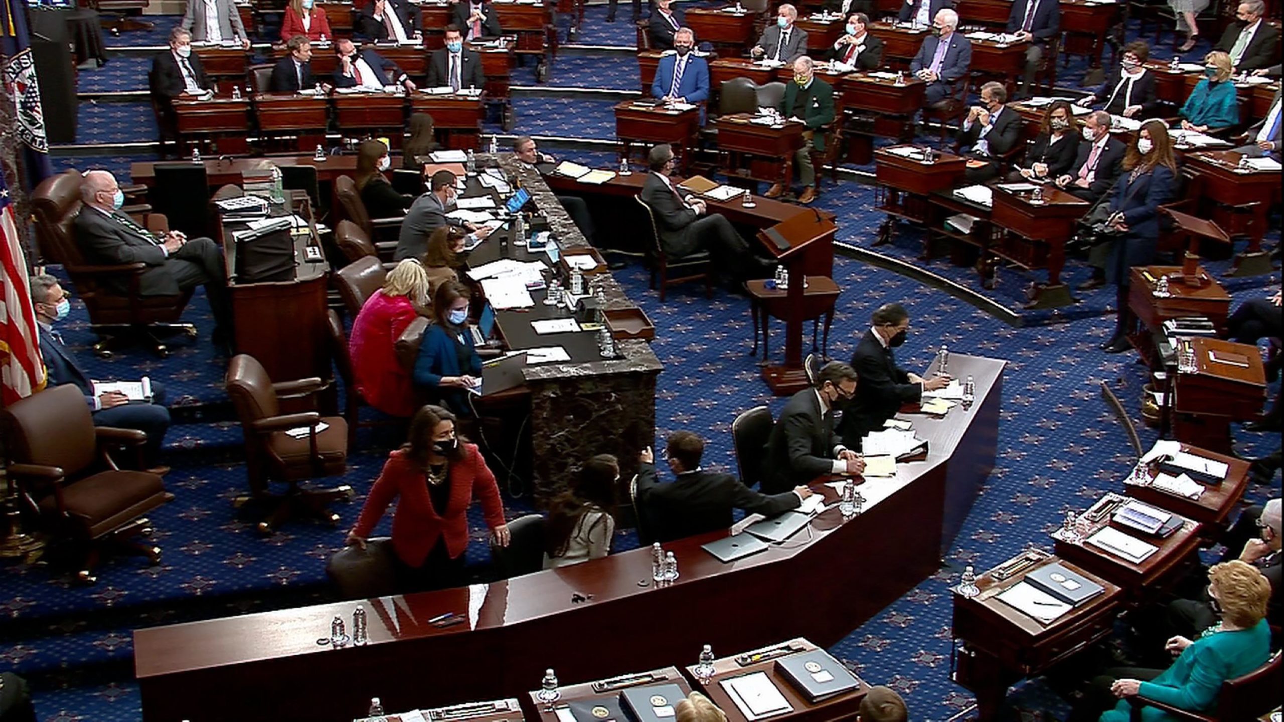 Image of a look inside the impeachment trial. Many people sitting at desks reviewing documents.