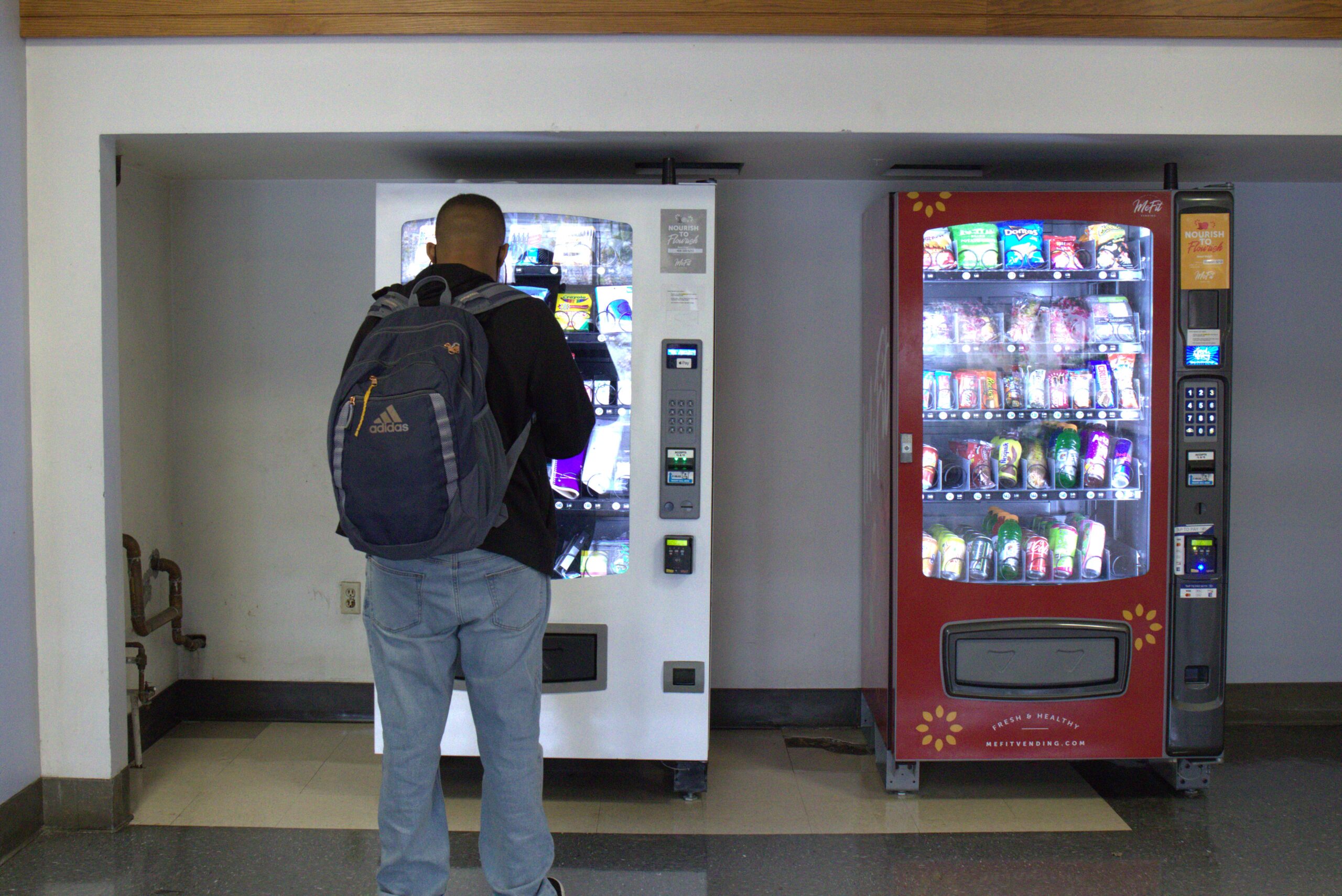 A male African-American student stands in front of the school supplies vending machine.