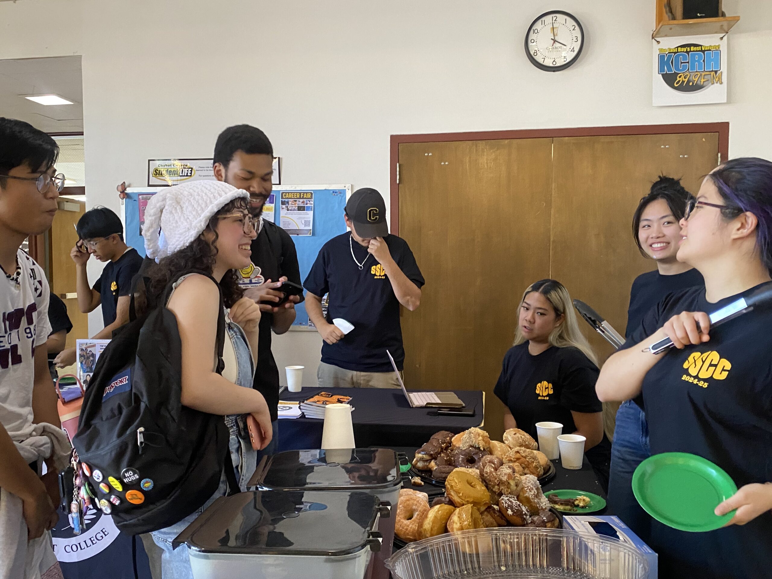 Students gathers around a table talking and taking free donuts