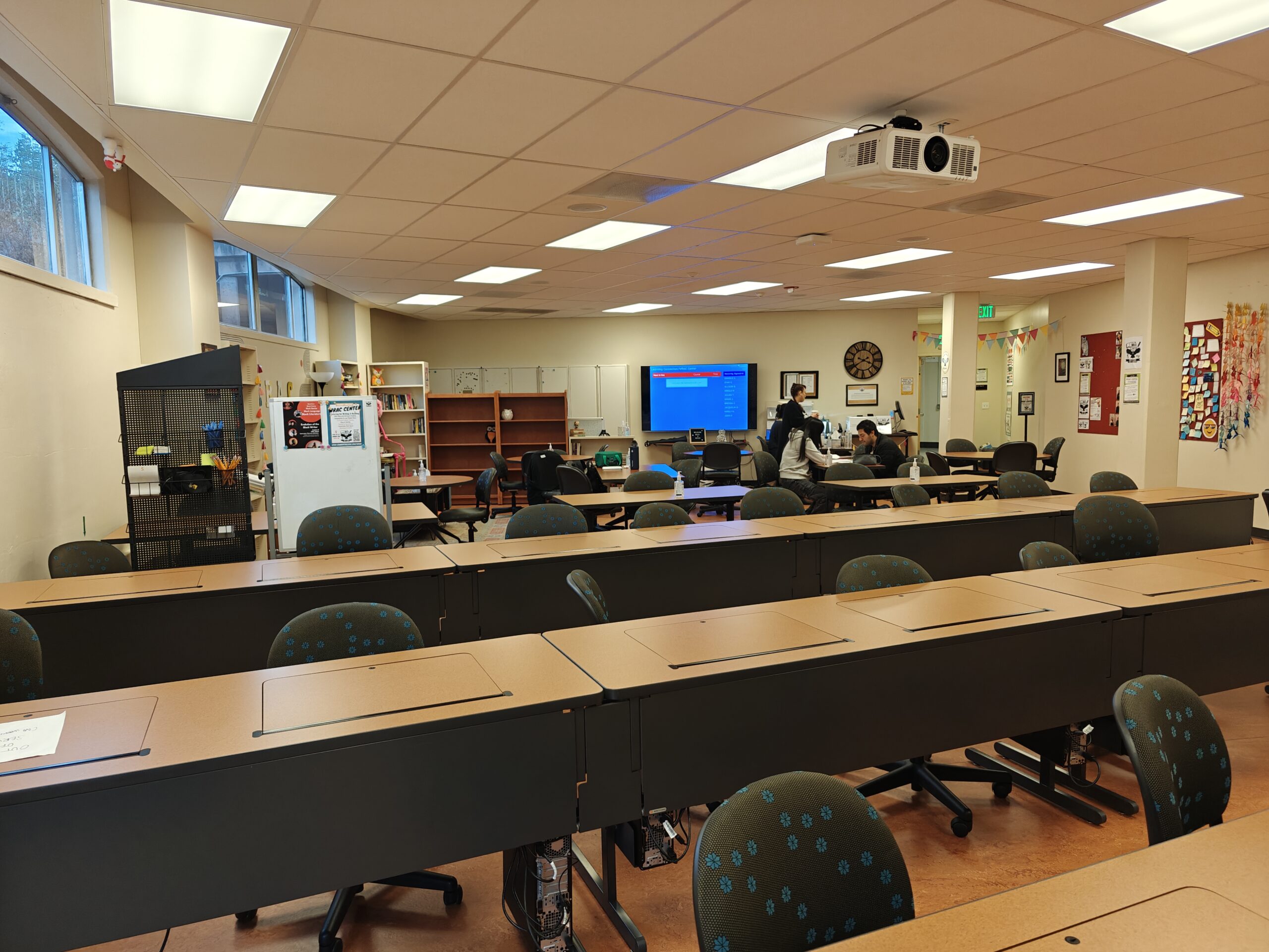 The inside of the WRAC Center room at Chabot College. The image contains Rows of long tables and seating with a large computer screen and smaller circular tables behind them.