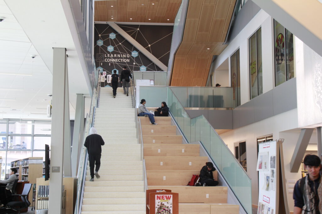 Image displays the new library's bookshelf with students walking up and down of it / Photographed by Michael Sykes