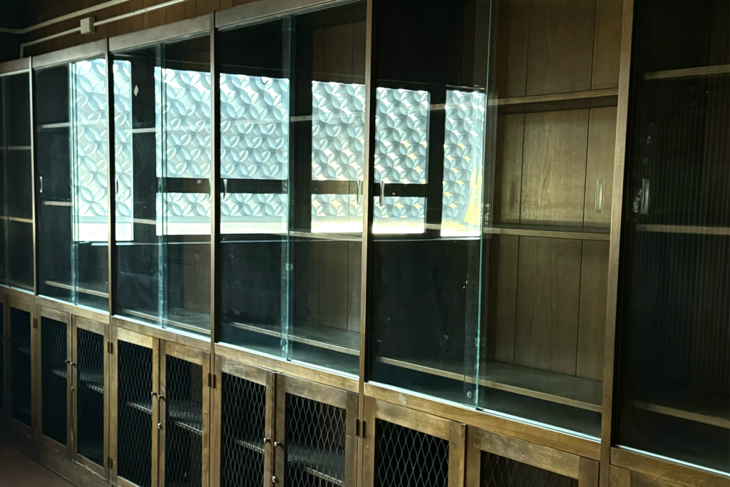 Image displays an old wooden wall length bookshelf with glass doors and see through cabinets /Photographed by Diana Cabrera